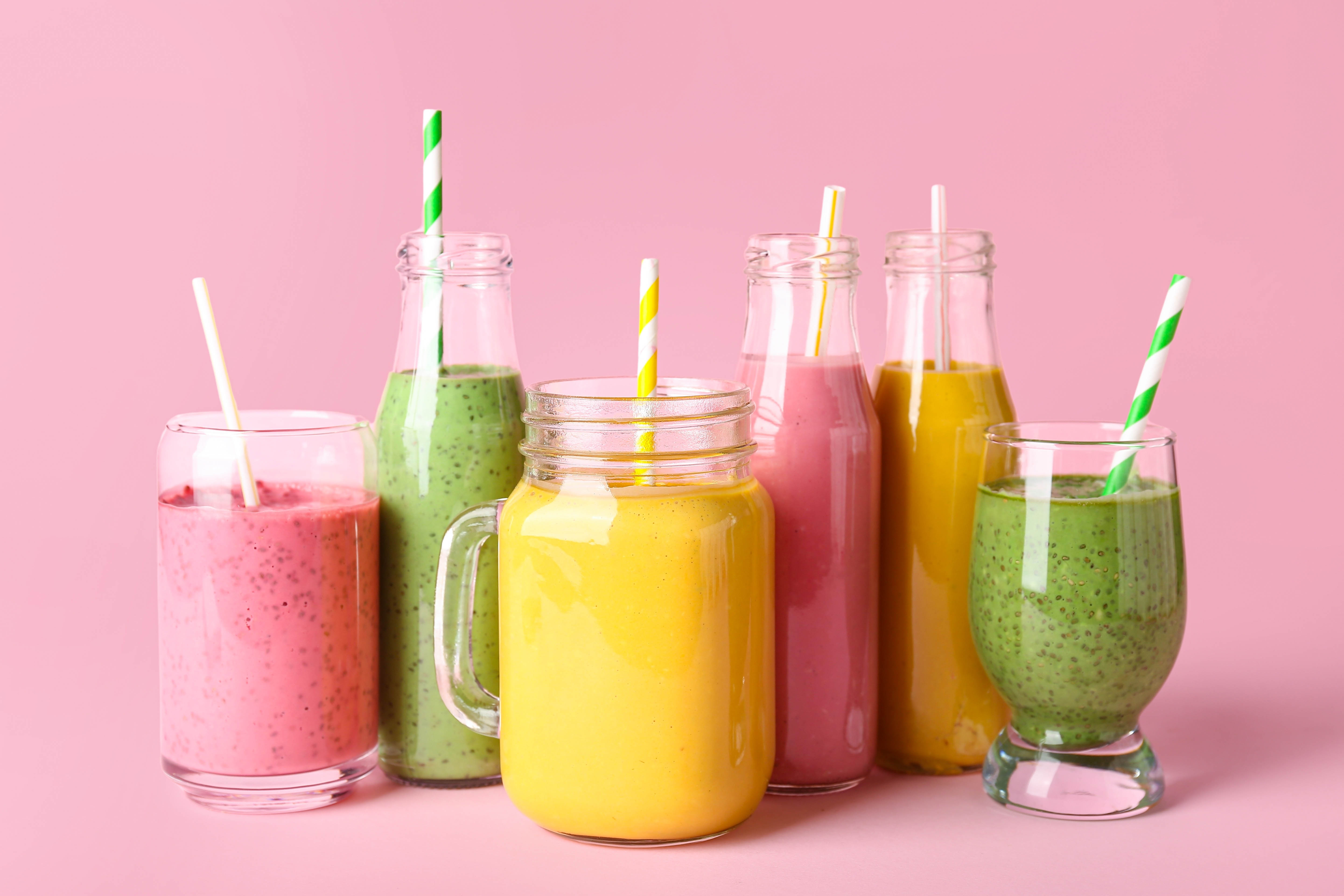 Various brightly coloured smoothies on a bright pink background